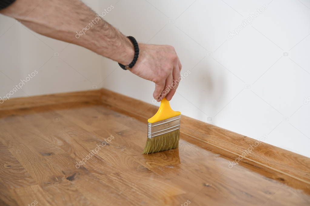  Varnishing lacquering parquet floor by paintbrush - second layer. Home renovation parquet. Varnish paintbrush strokes on a wooden parquet. Application of a highly glossy parquet lacquer