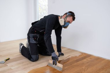 Eldivenleri ile marangoz ustası ahşap parke gruplandırıyor, zımparalamadan sonra. Meşe parke zeminini cilalayan, el ve spatula kullanan erkek işçiler.