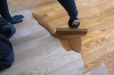 Eldivenli işçi ahşap parke gruplandırıyor, zımparalamadan sonra aşama aşama. Meşe parke zeminini cilalayan, el ve spatula kullanan erkek işçiler.