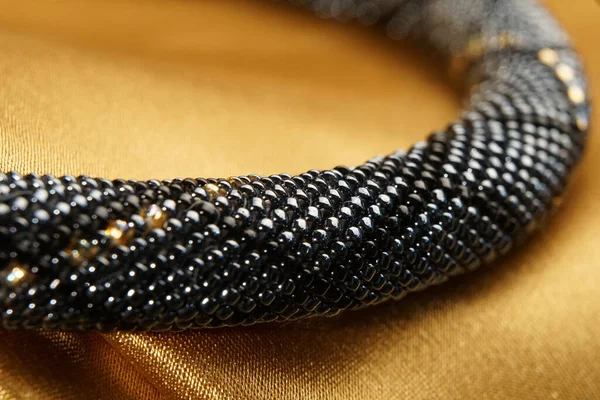 Close up of bead rope, seed beads, bead necklace. Black bead necklace on a gold satin