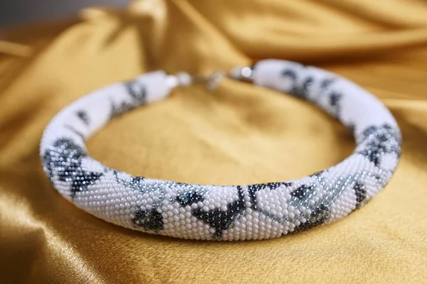 Close up of bead rope, seed beads, bead necklace. White bead necklace on a gold satin