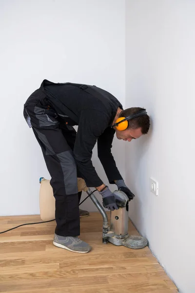 Scraping floor surface with grinding machine. Repair in the apartment. Carpenter grinder parquet in a narrow corner with a small machine — Stock Image Scraping Floor Surface Grinding Machine Repair Apartment Carpenter Grinder Parquet Stock Picture