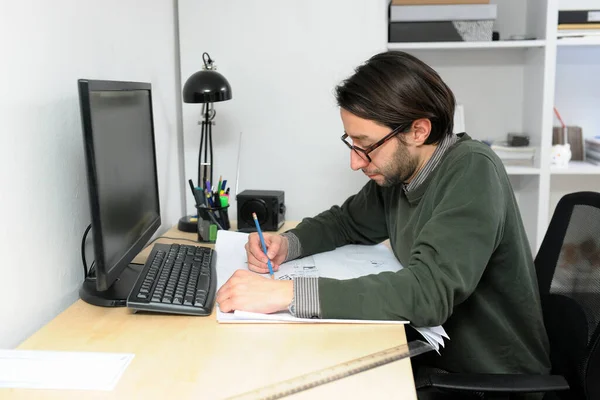 身穿休闲装的年轻建筑师男性在办公室里工作 在笔记本电脑上打字 桌子上摆放着设计图 — 图库照片