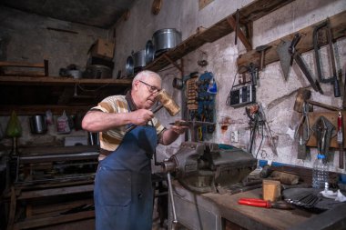 Atölyesinde metal levha ile çalışan yaşlı bir adam. Bir işçi metal levha ile dikkatli çalışır.