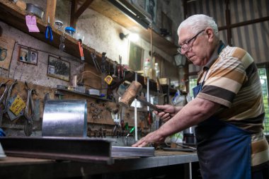 Atölyesinde metal levha ile çalışan yaşlı bir adam. Bir işçi metal levha ile dikkatli çalışır.