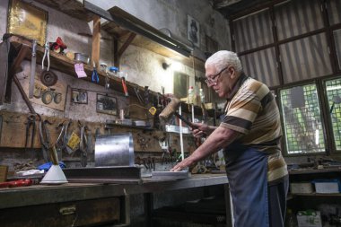 Atölyesinde metal levha ile çalışan yaşlı bir adam. Bir işçi metal levha ile dikkatli çalışır.