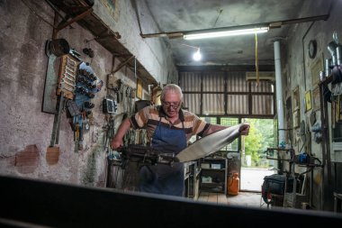 Atölyesinde metal levha ile çalışan yaşlı bir adam. Bir işçi metal levha ile dikkatli çalışır.