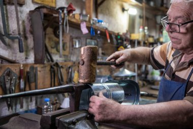 Atölyesinde metal levha ile çalışan yaşlı bir adam. Bir işçi metal levha ile dikkatli çalışır.