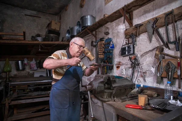 Atölyesinde metal levha ile çalışan yaşlı bir adam. Bir işçi metal levha ile dikkatli çalışır.