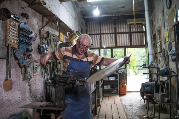 Atölyesinde metal levha ile çalışan yaşlı bir adam. Bir işçi metal levha ile dikkatli çalışır.