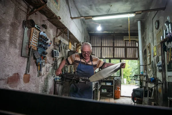 Atölyesinde metal levha ile çalışan yaşlı bir adam. Bir işçi metal levha ile dikkatli çalışır.