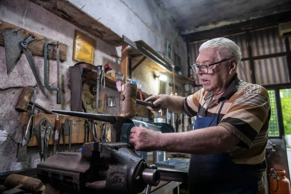 An older man working with sheet metal in his workshop. A worker works carefully with sheet metal