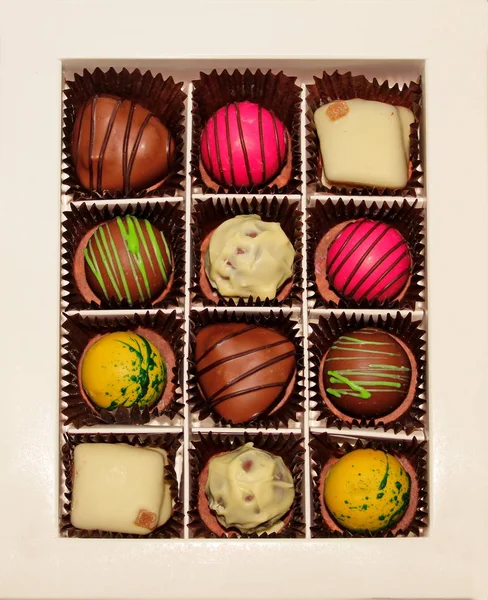 Gift box of handmade chocolates different form on white background. Twelve bright appetizing colored (pink, white, yellow, brown) candies. Glazed sweets with chocolate, nut, marzipan, caramel, praline filling. Festive treat for tea or coffee.