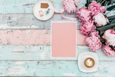 Güzel şakayık çiçekleri, fincan kahve ve pembe vintage zarfın üzerinde eski püskü ahşap masa arka plan
