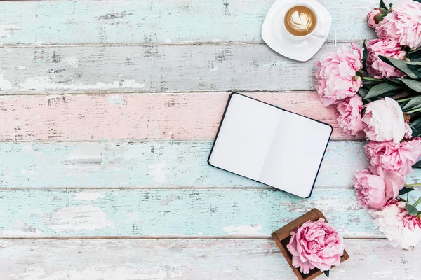 Flat lay home office desk.Pink peony bouquet, coffee and notebook on wooden background.Top view feminine. Flat lay home office desk. Woman workspace