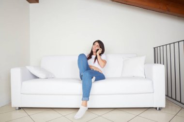 Güzel bir kadın koltukta cep telefonuyla konuşuyor.