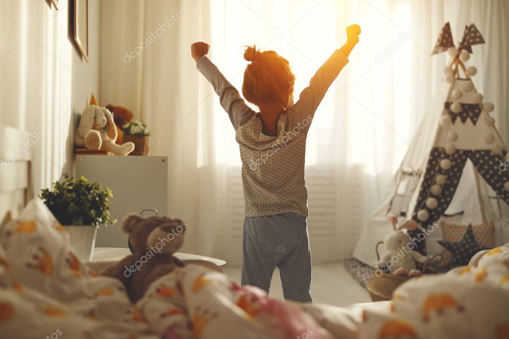 child girl wakes up in morning in bed and stretches by windo