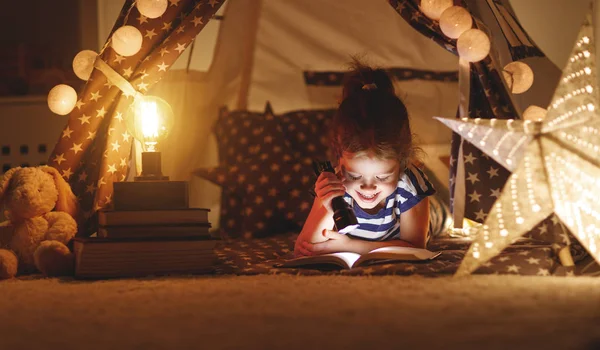 幸せな子女の子笑いとで紅テントの中で暗闇の中で本を読んで — ストック写真