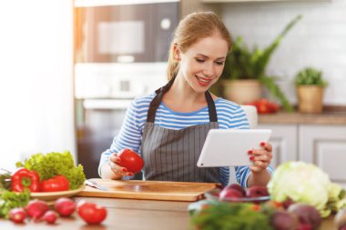 mutlu kadın bir tabloyla reçete üzerinde mutfakta sebze hazırlama