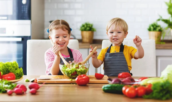 Healthy eating. Happy children prepares and eats vegetable salad in kitche