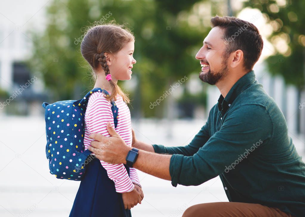 first day at school. father leads a little child school girl in first grad