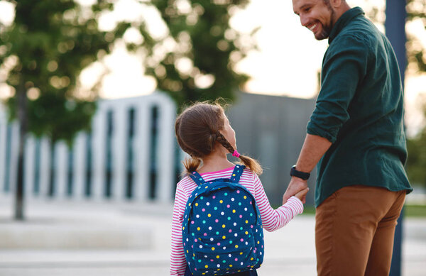 first day at school. father leads a little child school girl in first grad