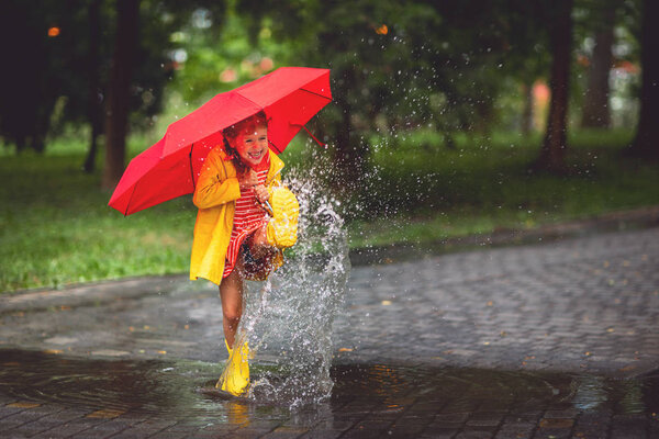 happy child girl with an umbrella and rubber boots in puddle on an autumn wal