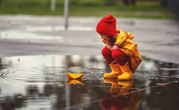 Natur で秋に水たまりに傘と紙のボートを持つ幸せな子少女 — ストック写真