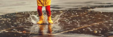 legs of child   with rubber boots jump in puddle on an autumn wal