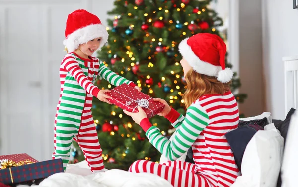 幸せな家族の母がクリスマス トレ近くクリスマスの朝にプレゼントを開くのパジャマを着て彼女の赤ん坊の息子を抱っこ — ストック写真