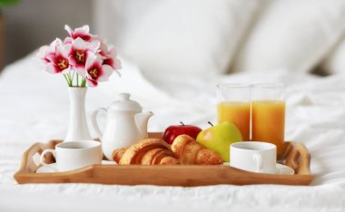 kahve, kruvasan, portakal suyu ve meyve bir tepsi üzerinde yatakta kahvaltı