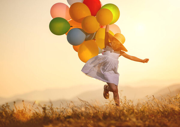 young happy child girl with balloons at sunset in summe