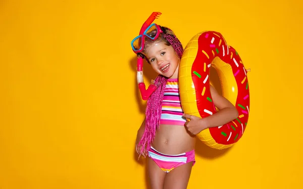 愉快的女孩在泳装与游泳圈甜甜圈在一个有色黄色背景 — 图库照片