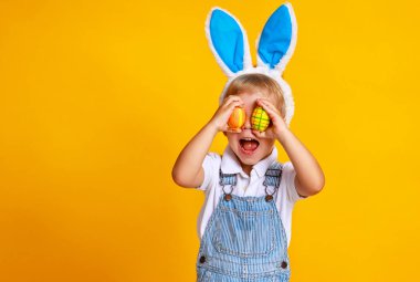 funny happy child boy with easter eggs and bunny ears on yellow backgroun clipart