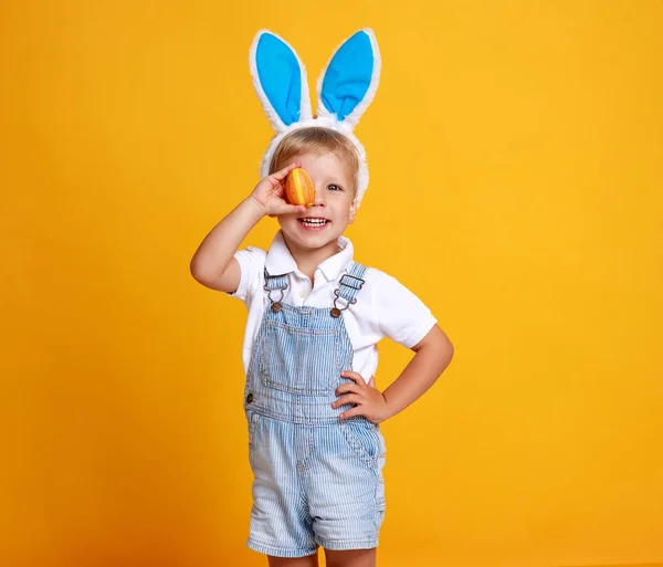 Divertido niño feliz con huevos de Pascua y orejas de conejo en amarillo — Foto de Stock