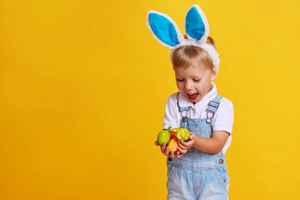 Rolig lyckligt barn pojke med påskägg och bunny öron på gula — Stockfoto