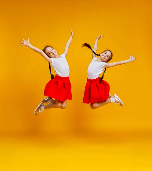 Grappige kinderen meisjes tweeling springen op gekleurde gele pagina — Stockfoto