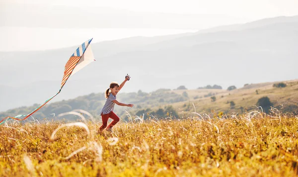 Счастливая девочка бегает с воздушным змеем на закате под открытым небом — стоковое фото