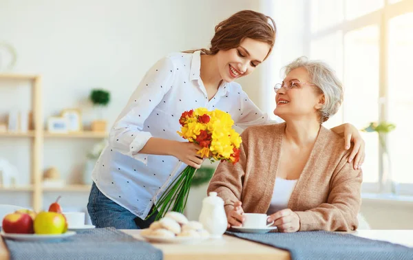 Glücklicher Muttertag! Erwachsene Tochter überreicht Blumen und gratuliert — Stockfoto