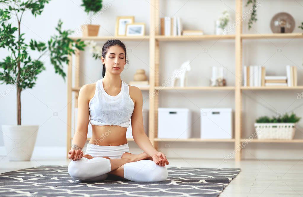 woman doing yoga, meditating in Lotus position at home    