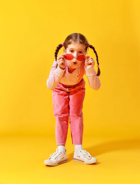 Смешной смешной ребенок девочка в розовой одежде на желтом фоне — стоковое фото