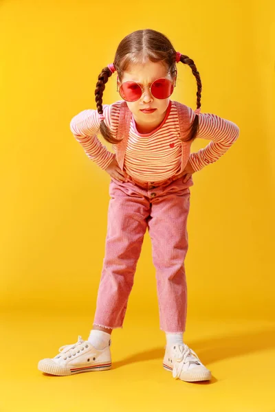 Engraçado engraçado criança menina em roupas rosa no fundo amarelo — Fotografia de Stock