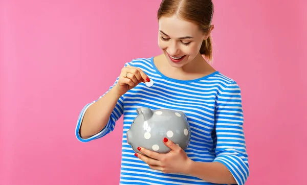 Счастливая женщина с копилкой денег на розовом фоне. финансы — стоковое фото