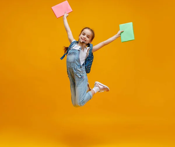 Смішна дівчинка школярка стрибає жовтим фоном — стокове фото