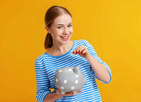 Lycklig kvinna med Piggy Money Bank på gul bakgrund. financia — Stockfoto