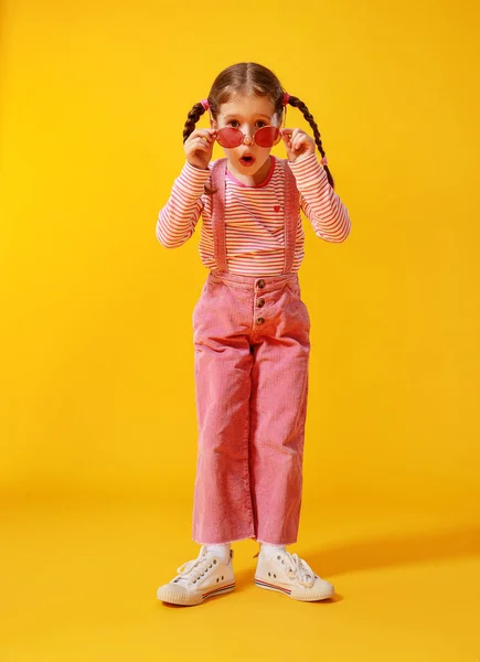 Engraçado engraçado criança menina em roupas rosa no fundo amarelo — Fotografia de Stock