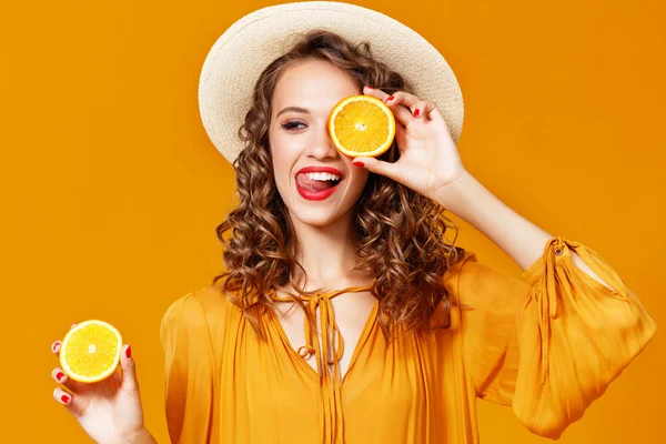 Cheerful young curly woman girl with   orange   on  yellow   bac — Stock Photo, Image