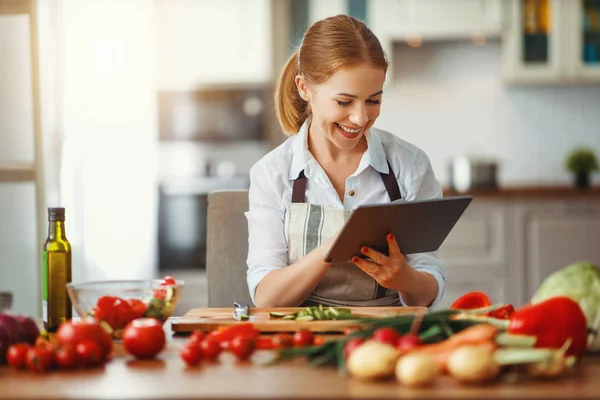 Lycklig kvinna förbereder grönsaker i köket på recept med — Stockfoto