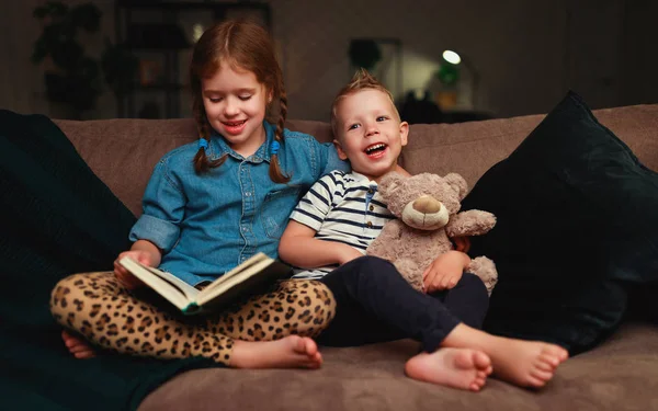 Niños felices niño y niña leyendo un libro en la noche en dar —  Fotos de Stock