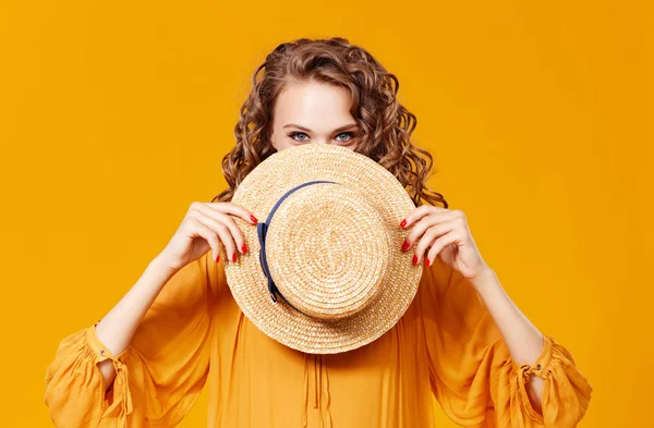 Bella giovane donna riccia in cappello estivo su sfondo giallo — Foto Stock